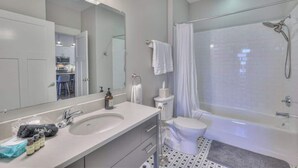 A modern bathroom with a large mirror, white sink, and a glass-enclosed shower area. - 1-BR Condo in 12 South I Unit 202 (Nashville)
