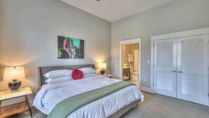 A bedroom with a bed, bedside lamps, a painting, a closet, and a bathroom visible through an open door. - 1-BR Condo in 12 South I Unit 202 (Nashville)