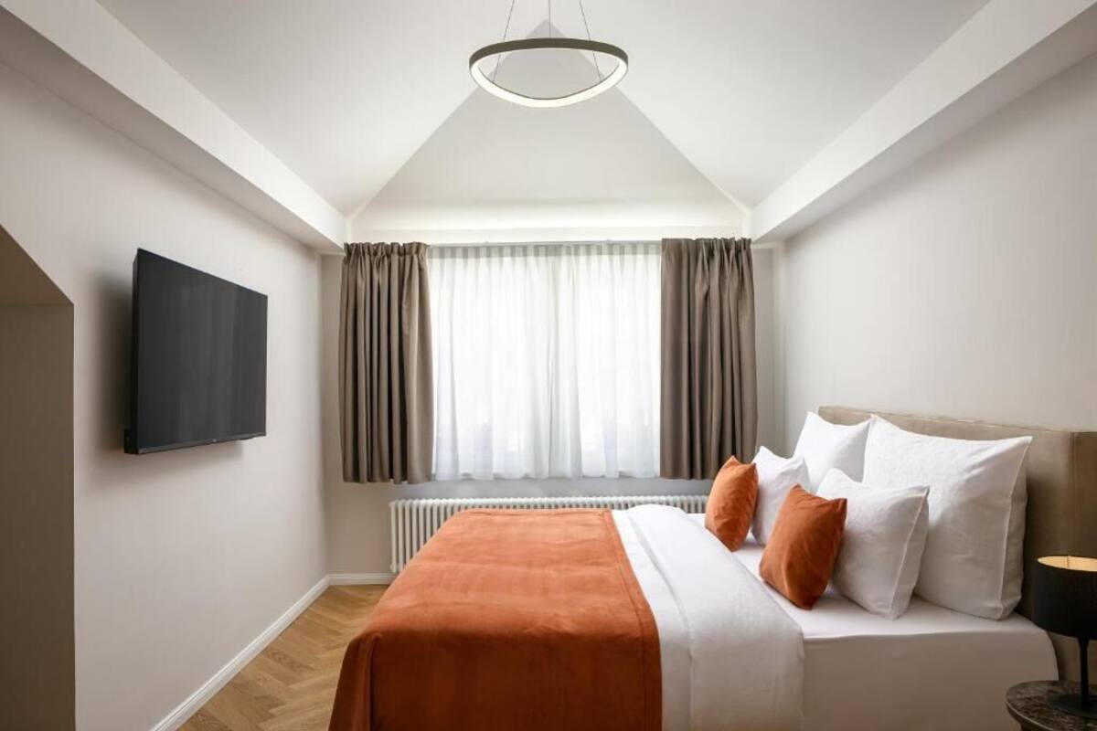 A modern bedroom with a bed, a flat-screen TV, a radiator, and a window with curtains.