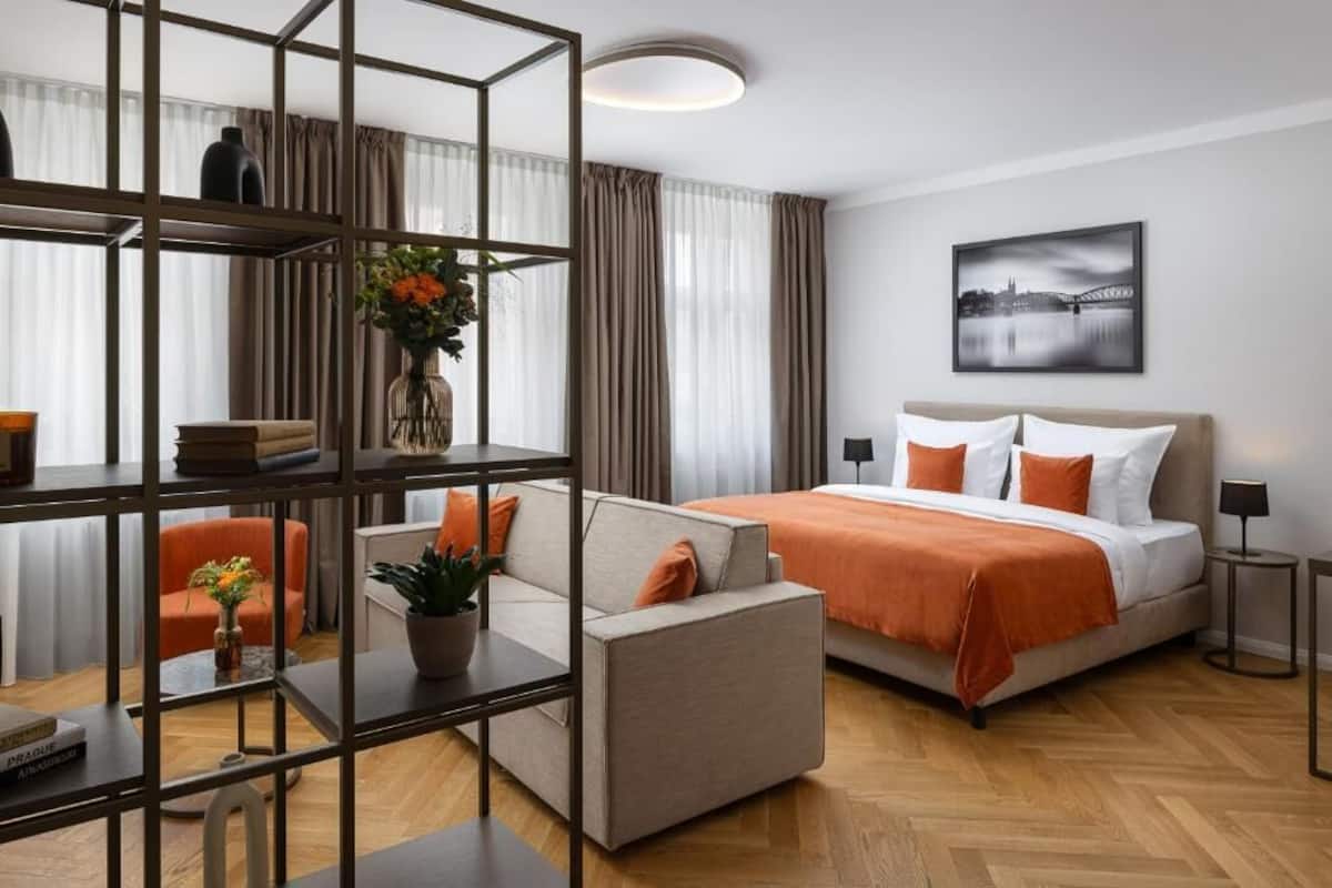 A modern hotel room with a bed, sofa, and a bookshelf.