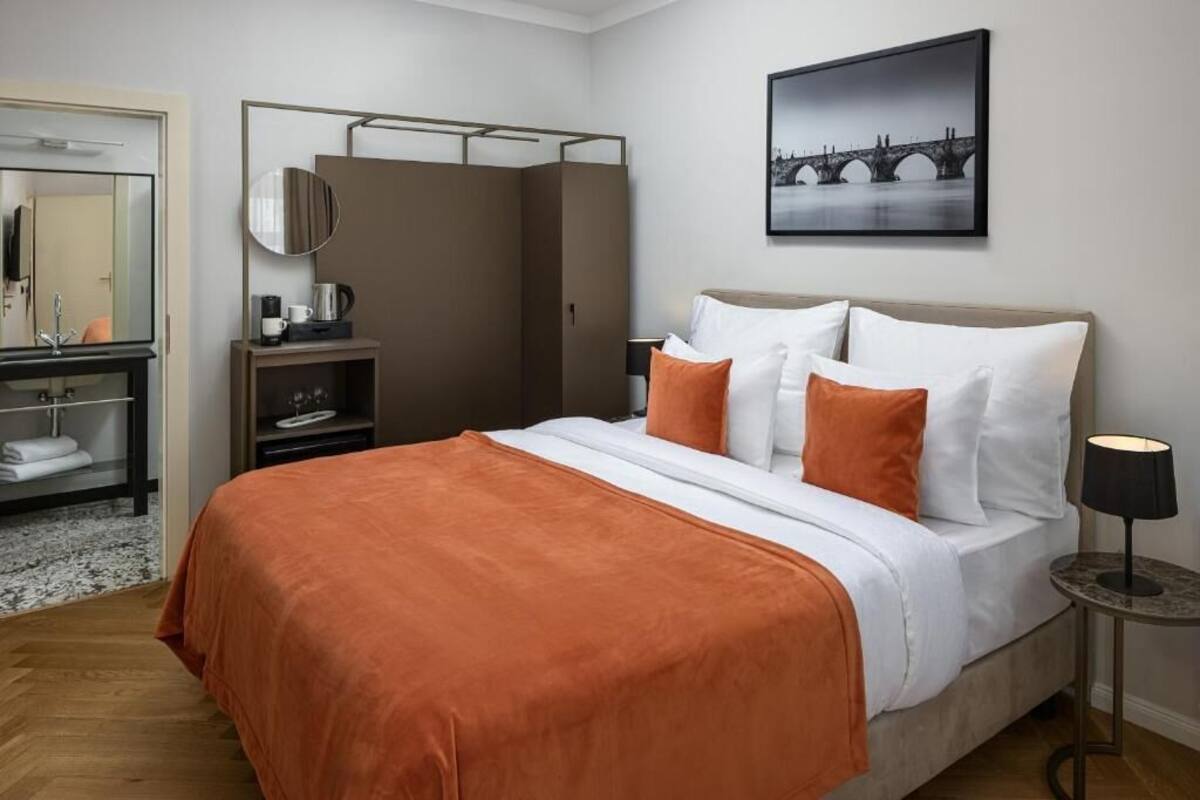A hotel room with a bed, a bedside table with a lamp, a wardrobe, a mirror, and a framed picture on the wall.