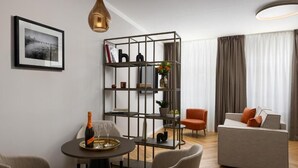 Ein modernes Wohnzimmer mit einem grauen Sofa, einem Esstisch mit einer Champagnerflasche und einem Metallregal an der Wand.