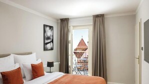 Ein Hotelzimmer mit Bett, Blick auf ein Gebäude und einem Balkon mit Tisch und Stühlen.