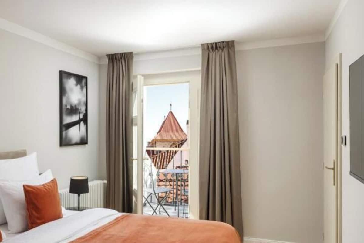 A hotel room with a bed, a view of a building outside, and a balcony with a table and chairs.