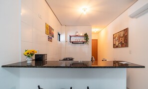 A modern kitchen with a black countertop, a gas stove, and a wall-mounted shelf with glassware and a clock. - Your Perfect Stay in Joao Pessoa, 220m From the sea - Rsks (João Pessoa)