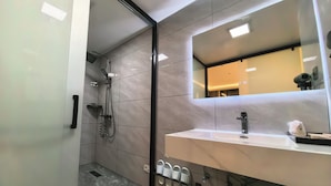 Een moderne badkamer met een douchecabine met glazen deur, een witte wastafel met een zwarte kraan en een spiegel erboven.