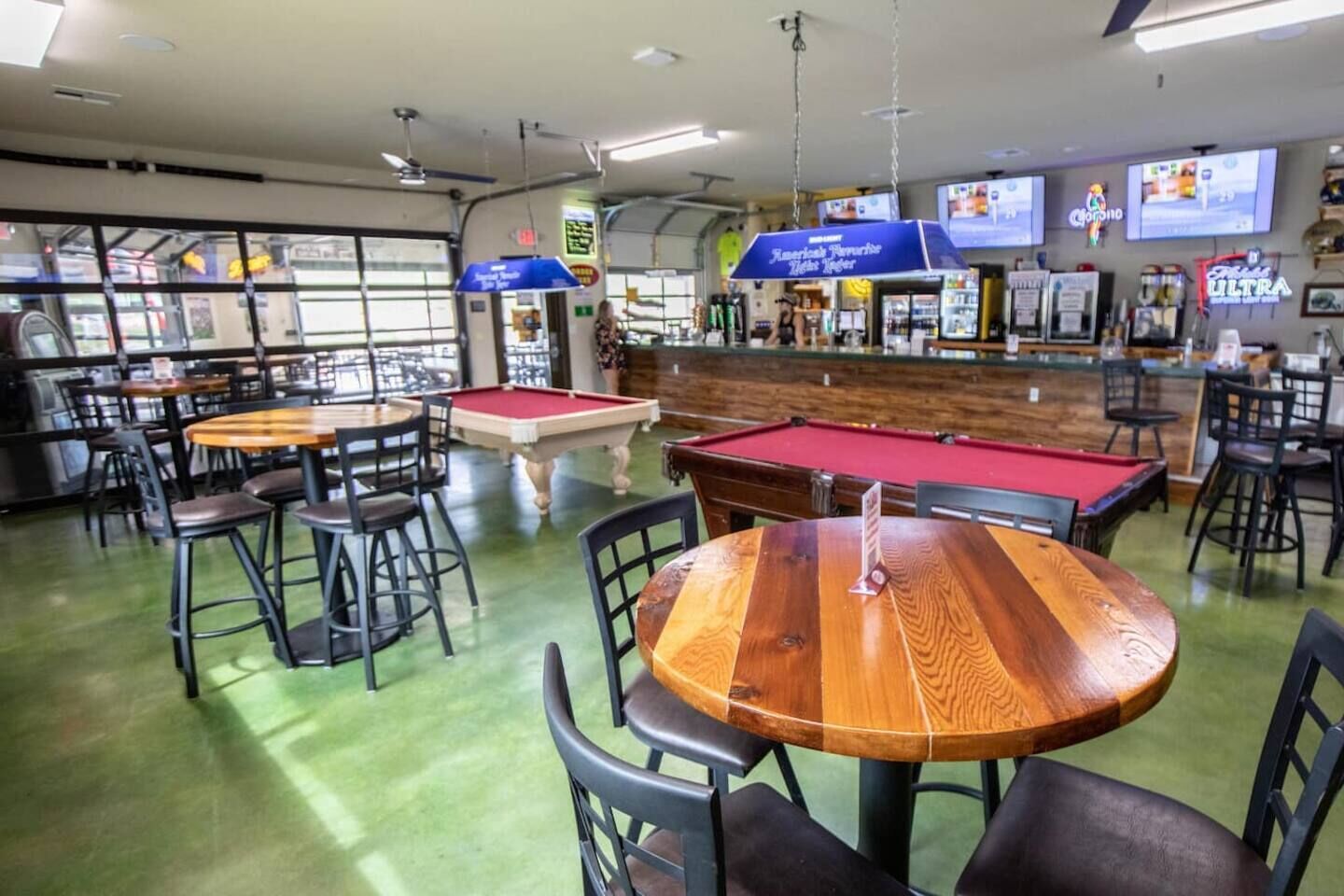 A billiards room with pool tables, chairs, and a bar area with TVs.