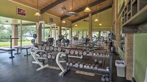 Ein Fitnessraum mit unterschiedlichen Trainingsgeräten, darunter Kurzhanteln und Kraftmaschinen, unter einer Holzbalkendecke mit hängenden Leuchten.