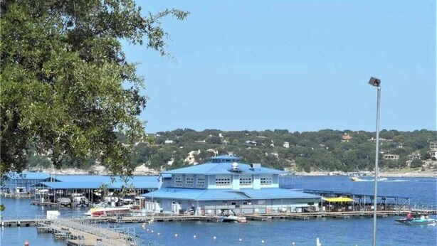 Ein Yachthafen mit vertäuten Booten, ein großes blaues Gebäude mit flachem Dach und eine Rasenfläche im Vordergrund.