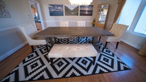 A dining area with a wooden table, white cushioned benches, a patterned rug, and a chandelier. - Private Resort! 100" Home Theater, HotTub, Pool, Basketball Court, extra games (Bowie)