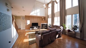 A spacious living room with a large sofa, a flat-screen TV, and a ceiling fan. - Private Resort! 100" Home Theater, HotTub, Pool, Basketball Court, extra games (Bowie)