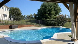 A swimming pool with a curved edge, surrounded by a concrete deck and a pergola. - Private Resort! 100" Home Theater, HotTub, Pool, Basketball Court, extra games (Bowie)