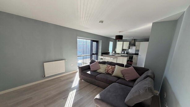 Un salon moderne avec un canapé gris, un radiateur et une vue sur la cuisine.