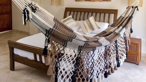 A hammock bed in a room with wooden beams, a hanging macrame decoration, and a wall painting. - Villa Arena (Isla de Margarita)