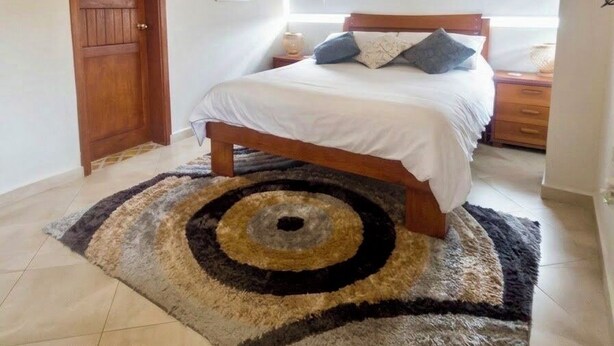 A bedroom with a wooden bed, a large circular rug, a wooden ceiling beam, and a hanging light fixture. - Villa Arena (Isla de Margarita)