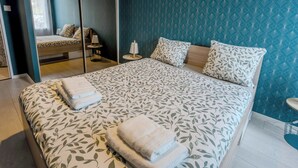A neatly made bed with a leaf-patterned bedspread, two pillows, and two folded towels. - Le Vigny – 24h du Mans – Wifi (Le Mans)