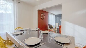 A dining area with a long table set for four, chairs, and a clock on the wall. - Le Vigny – 24h du Mans – Wifi (Le Mans)
