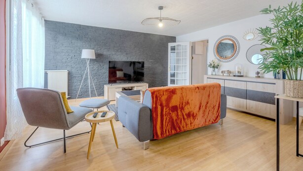 A modern living room with a grey sofa, a small table, and a TV. - Le Vigny – 24h du Mans – Wifi (Le Mans)