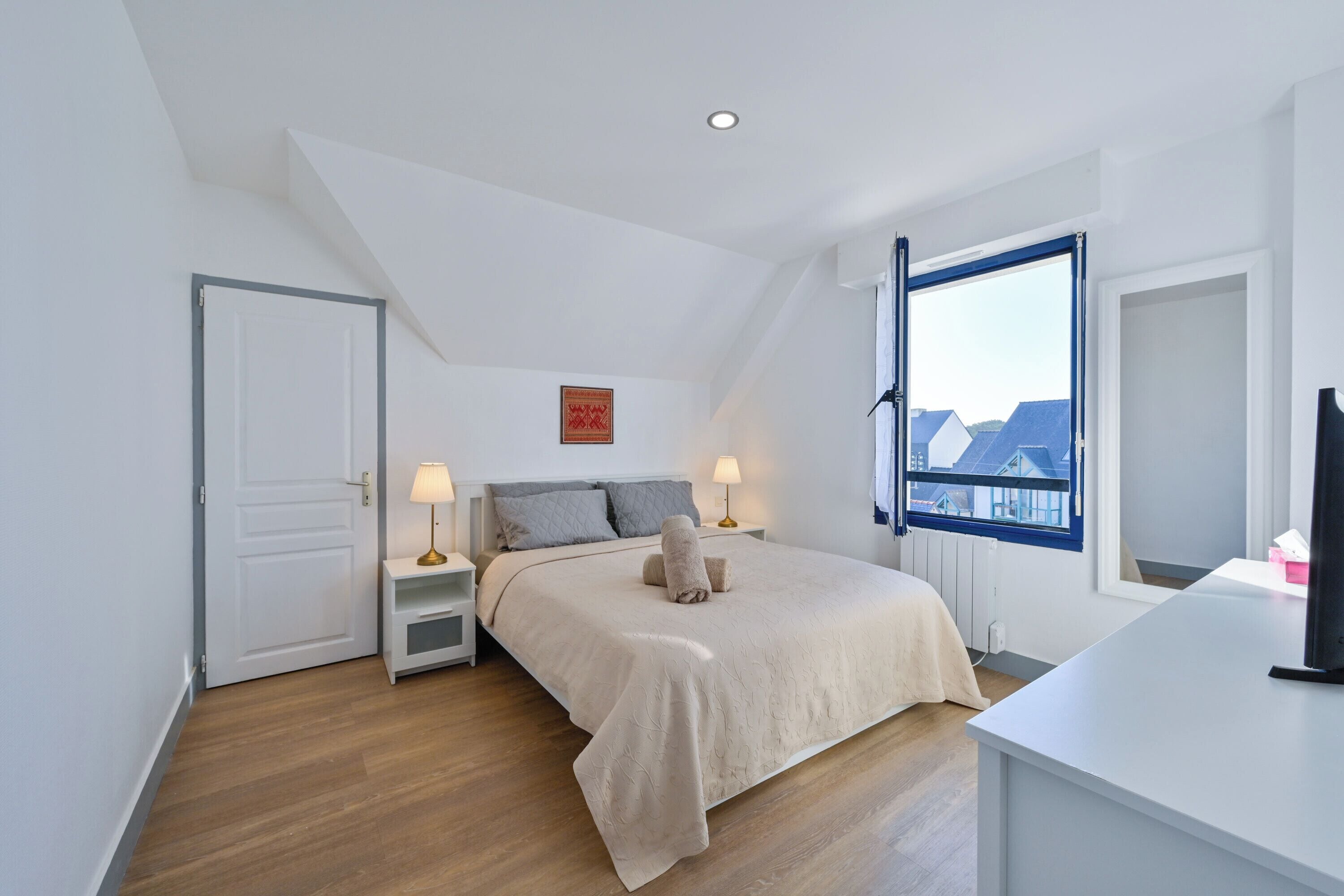 Une chambre à coucher avec un lit, des tables de chevet, une fenêtre et une vue sur des immeubles.
