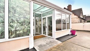 Un bâtiment moderne doté de grandes portes et fenêtres en verre, d’une entrée en béton et d’un seau rose posé sur le sol.