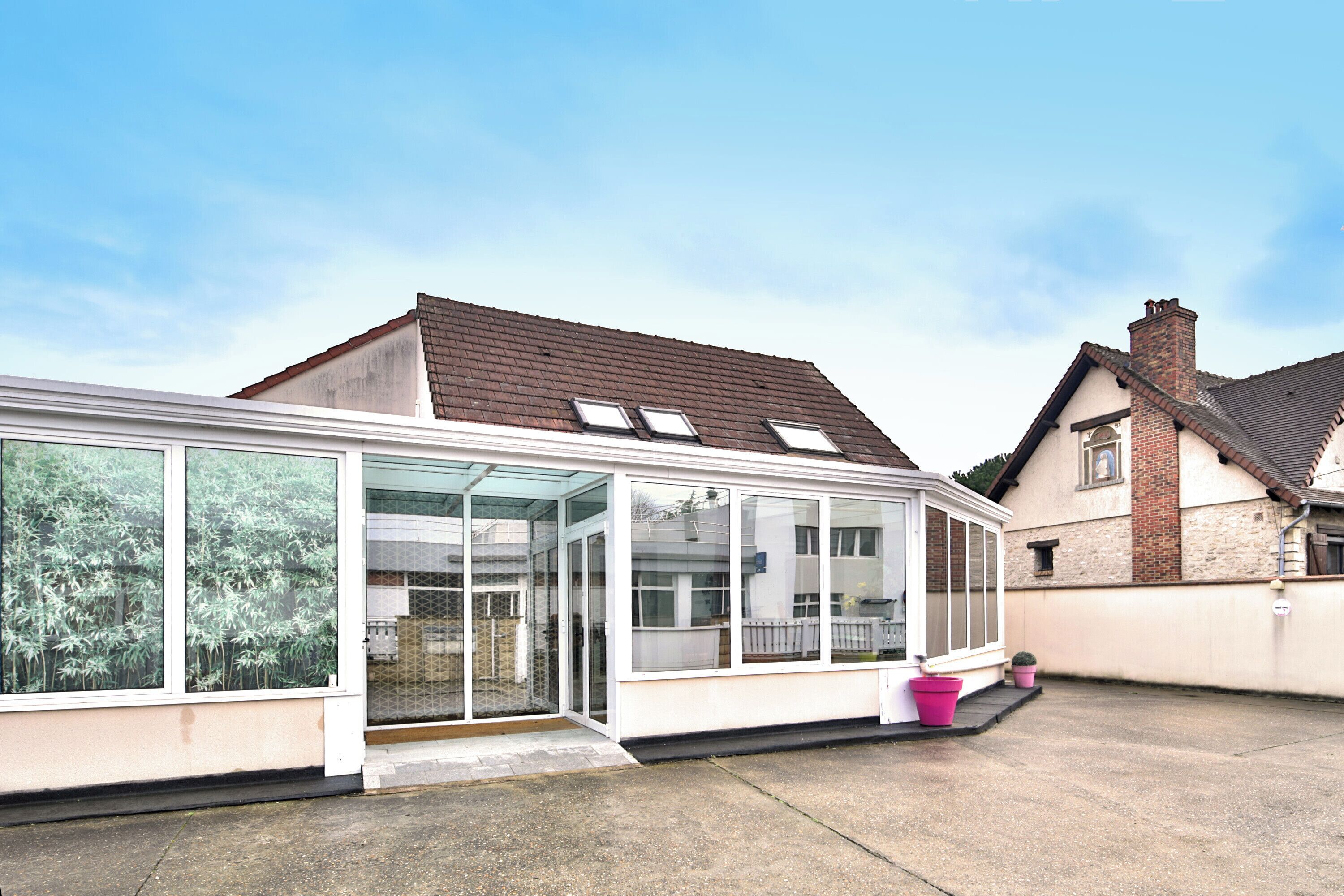 A conservatory with large glass doors, a small porch, and a brick house in the background.
