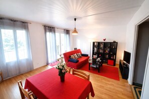 A living room with a red sofa, a black bookshelf, and a dining table with a red tablecloth. - Apartment 4 pers. 3 minutes from Clos Lucé (Amboise)
