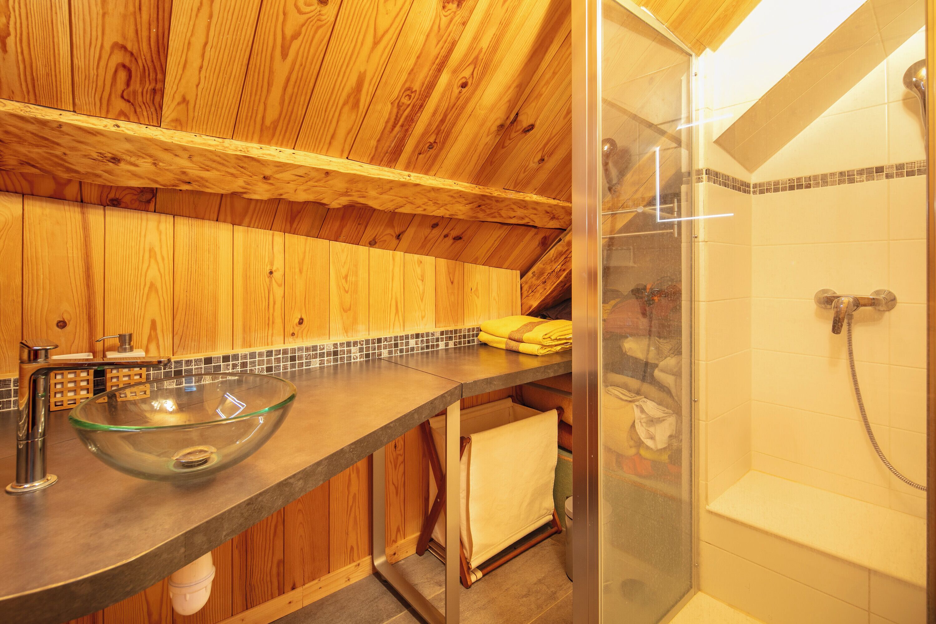 Een houten interieur met een glazen wastafel, een douche en een betegelde spatwand.