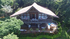 Une maison en bois à deux étages, dotée d’un balcon et entourée d’une végétation luxuriante.