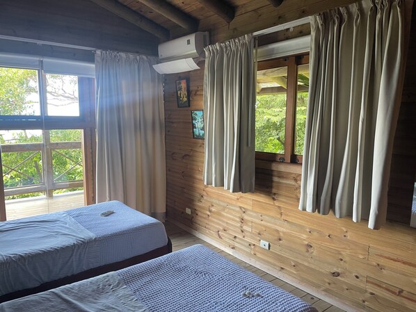 Une cabine avec deux lits, des murs en bois, une fenêtre avec des rideaux et un appareil de climatisation.