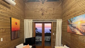 Une pièce chaleureuse aux murs en bois, dotée d’un ventilateur de plafond et offrant une vue sur la mer grâce à une porte vitrée.