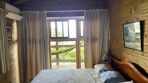 Une chambre avec un plafond en bois, un lit avec une literie blanche, une tête de lit en bois, un tableau encadré au mur et une fenêtre avec des rideaux.