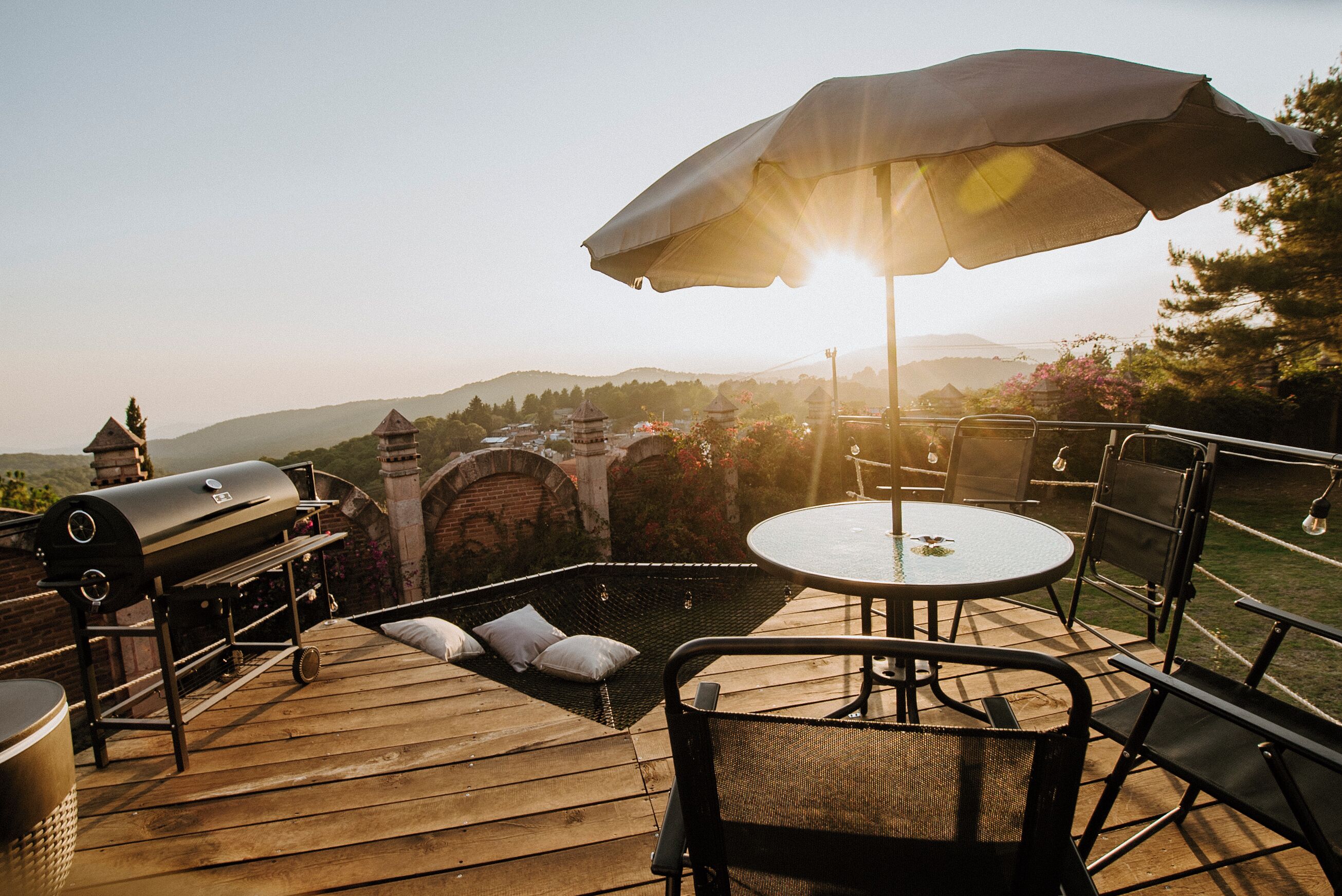 A wooden deck with a grill, a round table, and chairs, overlooking a mountainous landscape.