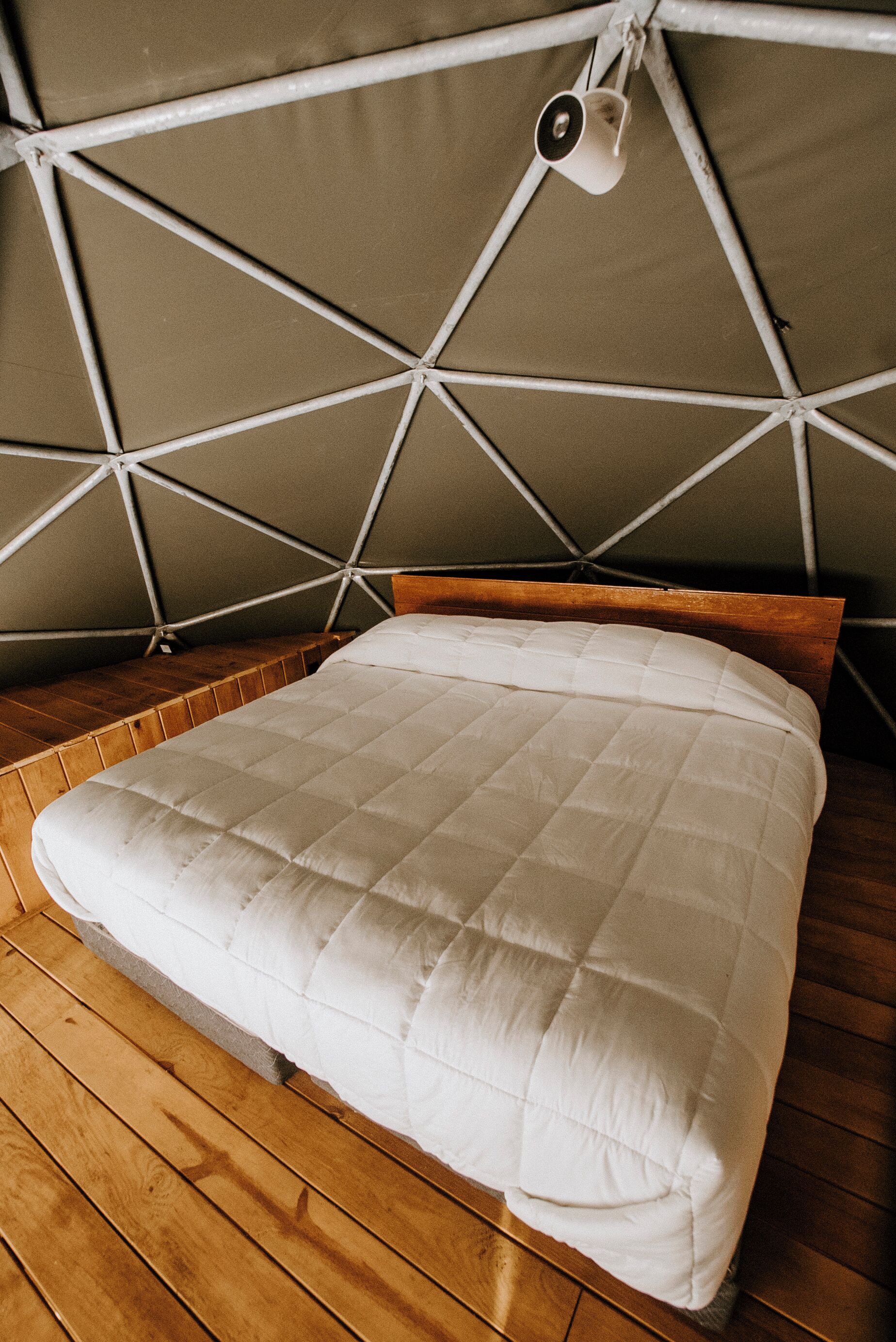 A tent-style room with a bed, wooden flooring, and a hanging light fixture.