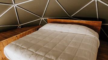 A tent-style room with a bed, wooden flooring, and a hanging light fixture.