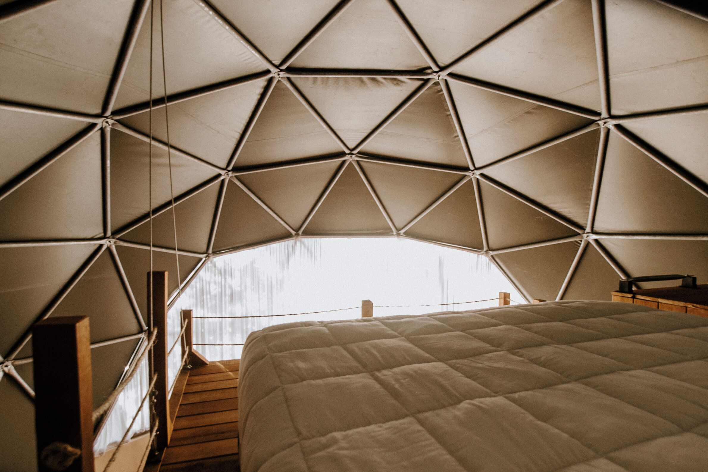 Una estructura tipo tienda de campaña con una cama en su interior, barandillas de madera y vistas al exterior.