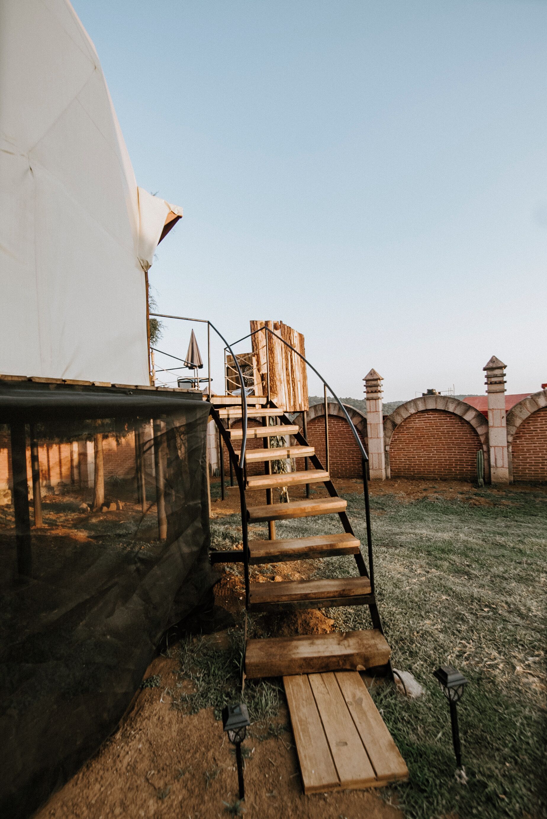 A tent with a wooden staircase leading to a covered area, surrounded by brick walls and a clear sky.