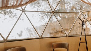 A room with a large window, two chairs, a wooden table, and a floor lamp. - LUMBAI GLAMPING MAZAMITLA (Mazamitla)