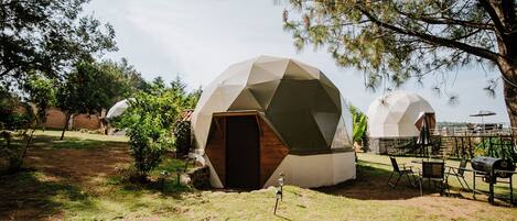 Geodesic dome structures with a wooden door, outdoor seating, and a grill area.