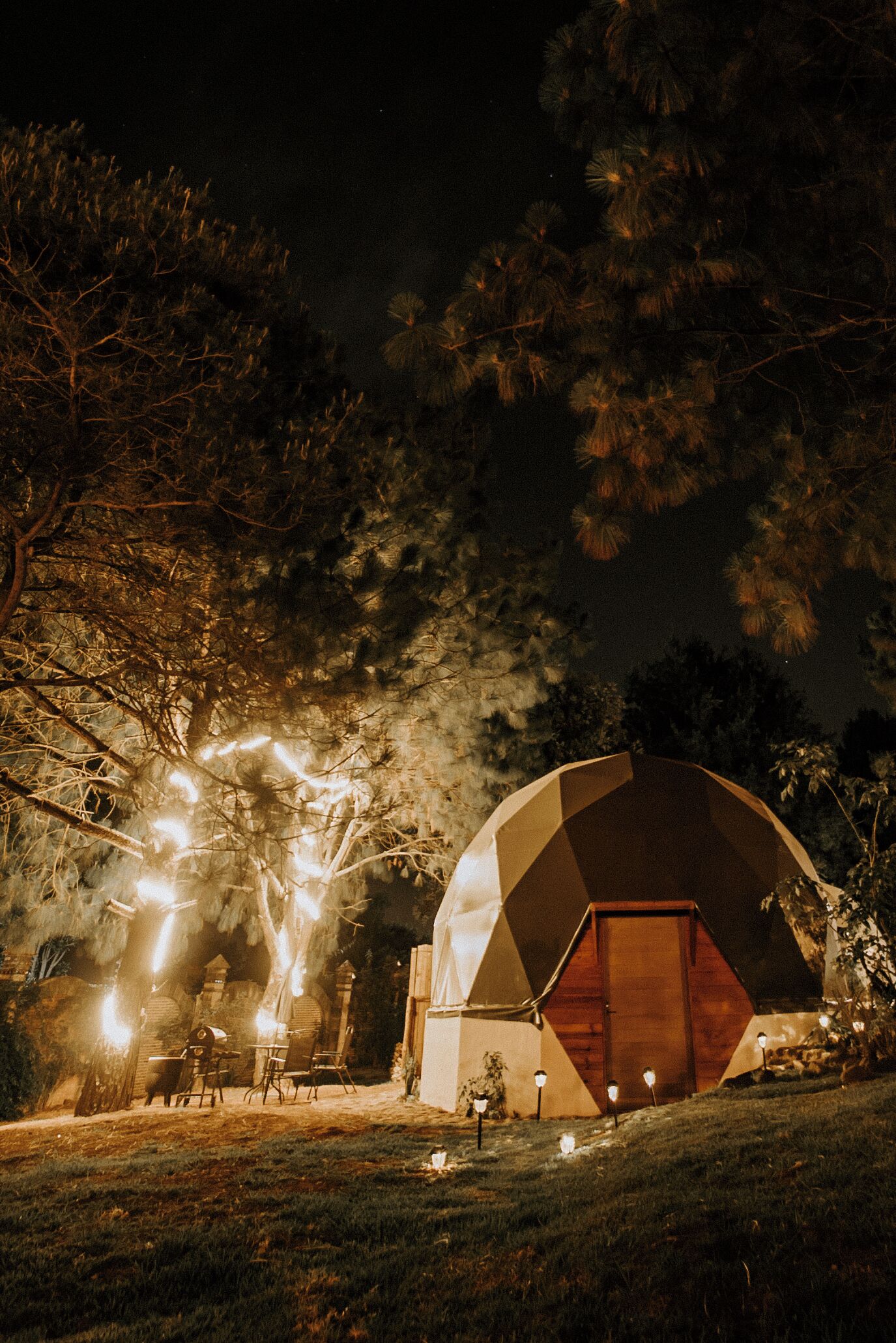A large, dome-shaped building with a wooden door, surrounded by trees and outdoor lighting.
