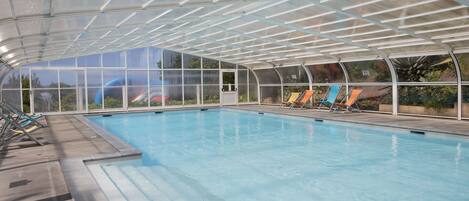 Une piscine intérieure dotée d’un toit en verre, d’une eau cristalline et de plusieurs chaises longues.