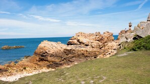 A coastal landscape with rocky formations, a grassy area, and a lighthouse. - Cap - Confort 2 TV - 4/5p (Plouézec)
