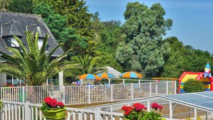 A pool area with a white fence, a slide, and colorful umbrellas. - Cap - Confort 2 TV - 4/5p (Plouézec)