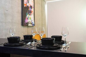 Une table à manger dressée avec des bols noirs et des verres à vin, et une peinture abstraite aux couleurs vives en arrière-plan.
