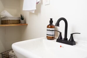 Un lavabo de salle de bain avec un robinet noir, un flacon de savon liquide et un distributeur de savon CATO.