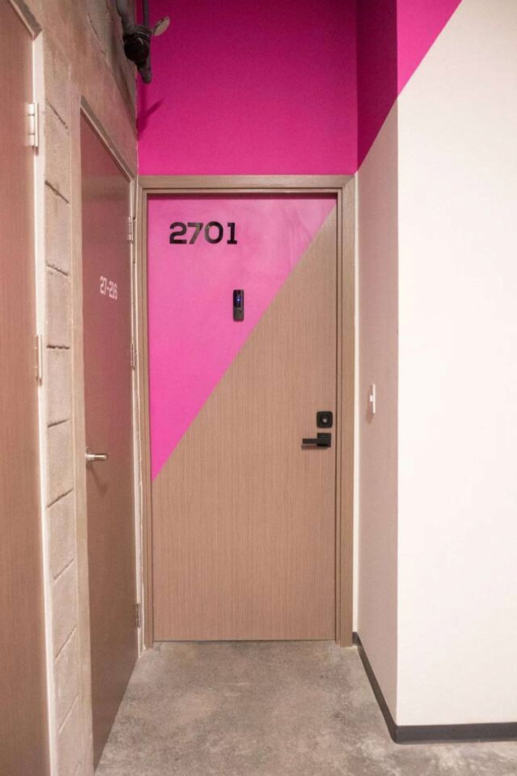 Un pasillo con una puerta marcada 2701, una pared rosa y un marco de puerta de madera.