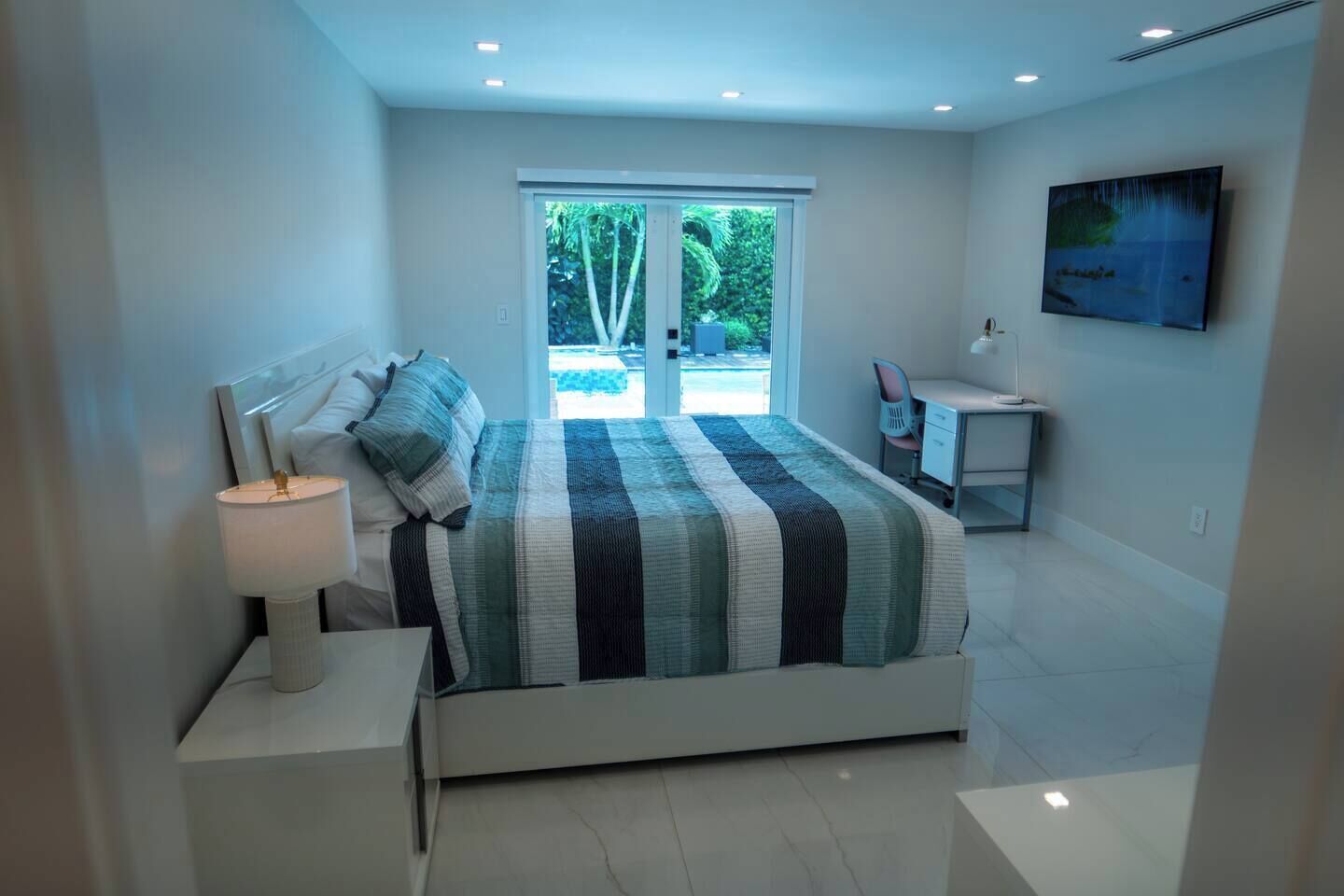 Een moderne slaapkamer met een groot bed, een bureau en uitzicht op een zwembad.