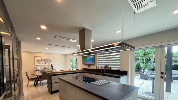 A modern kitchen with a central island, a dining area with a table and chairs, and a large window providing a view of the outdoors. - Greenview Villa/Luxury Heated Pool Home Golf View (Miami)