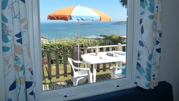 Uma janela com vista para o mar, uma mesa com cadeiras e um guarda-sol.