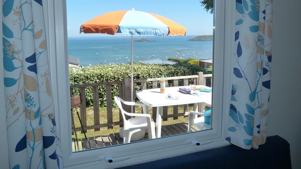 A window with a view of the sea, a table with chairs, and an umbrella. - Cap - Confort 2 TV - 4/5p (15) (Plouézec)