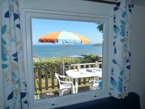 A window with a view of the sea, a table with chairs, and an umbrella. - Cap - Confort 2 TV - 4/5p (17) (Plouézec)